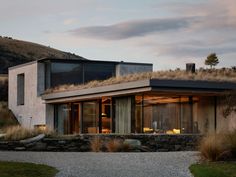 a modern house with grass on the roof and stone walls, overlooking a grassy hillside