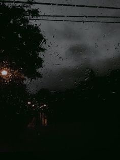 rain drops on the windshield of a car as it drives down a street at night