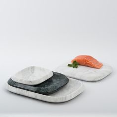 two plates with salmon on them sitting side by side, one is black and the other is white