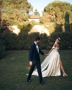 a bride and groom holding hands in the grass with trees behind them on their wedding day