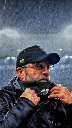 an older man wearing a hat and glasses in the rain with his hand on his shoulder