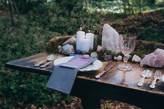 a table set with candles, plates and utensils for a wedding reception in the woods