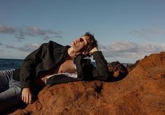 a young man laying on top of a rock next to the ocean with his eyes closed