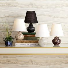 three lamps sitting on top of a table next to books and vases with plants