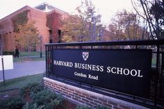 a sign for the harvard business school in front of a brick building with trees around it