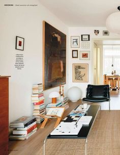 a living room filled with furniture and pictures on the wall next to a table covered in books