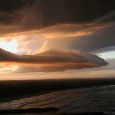 a large cloud hangs over the ocean at sunset