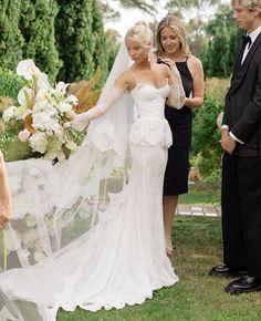 the bride is walking down the aisle with her veil blowing in the wind as two other people look on