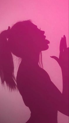 the silhouette of a woman holding her hands up in front of a pink sky background