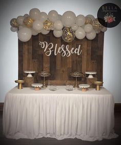 a table topped with white balloons and gold candles next to a sign that says blessing