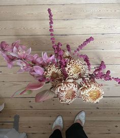 a person standing next to a bunch of flowers on top of a wooden floor with their feet in the air