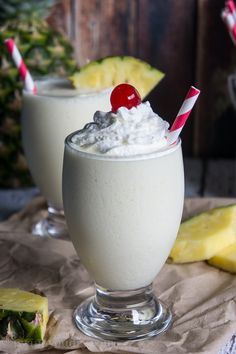 two glasses filled with milkshakes sitting on top of a table next to pineapple slices