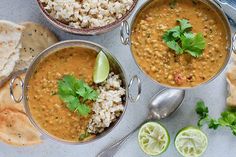 three bowls filled with soup next to some pita bread and lime slices on the side