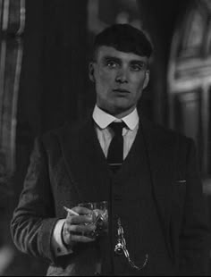 a man in a suit and tie holding a glass with something in his right hand