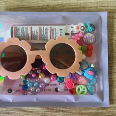 a pair of pink sunglasses sitting on top of a plastic bag filled with beads and other items