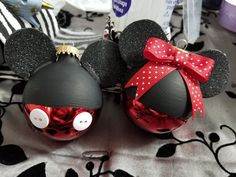 two mickey and minnie mouse christmas ornaments on a table with black and red decorations in the background