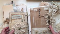 two hands are holding an open book with lace and buttons on it, surrounded by other handmade items