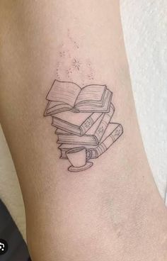 a stack of books tattoo on the arm with coffee cup and book in front of it