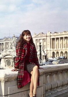 a woman sitting on top of a stone wall next to a bridge with buildings in the background