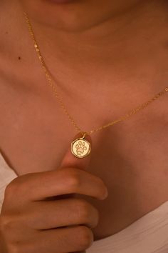 a woman wearing a gold necklace with a small medallion on it's center piece