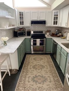 a kitchen with green cabinets and white counter tops, an area rug on the floor