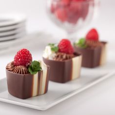 three small desserts with chocolate and raspberries are on a white platter