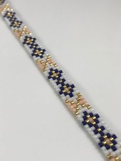 a white and blue bracelet with gold accents on the end, sitting on top of a table