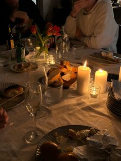 people sitting at a table with food and wine in front of them, candles on the plates