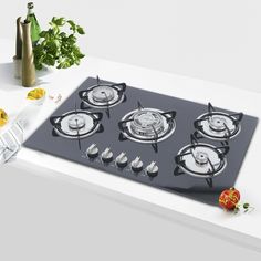 a stove top with four burners sitting on a counter next to vegetables and wine bottles