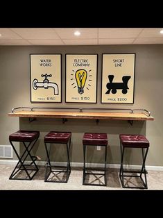 three framed posters on the wall above stools in a room with carpeted flooring