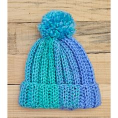 a blue and green knitted hat sitting on top of a wooden table