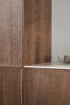 an empty glass sits on top of a wooden cabinet next to a white countertop