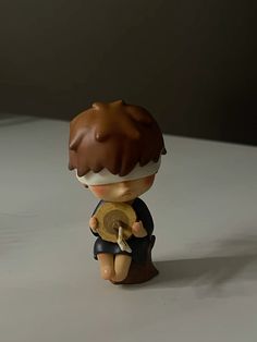 a little boy figurine sitting on top of a white table next to a cup