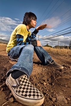 a young man sitting on top of a dirt field next to power lines and telephone poles