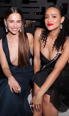 two beautiful young women sitting next to each other at a fashion show in black dresses