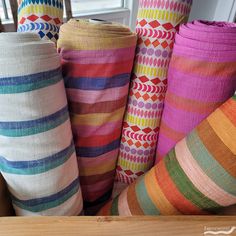 many colorful rolls of fabric sitting on top of a wooden table next to a window