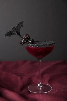 a halloween drink garnished with blackberries and sprinkles sits on a red cloth