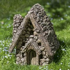 a small house made out of rocks sitting in the middle of some grass and flowers