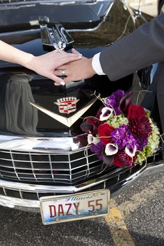 the bride and groom are holding hands on the hood of their classic car, which is decorated with flowers