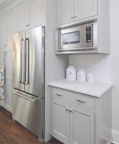 a stainless steel refrigerator and microwave in a white kitchen with wood floors, cabinets and drawers