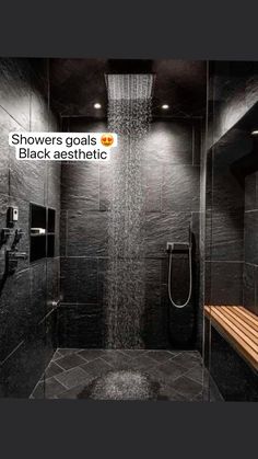 a shower head in the middle of a black tiled bathroom with wooden bench under it