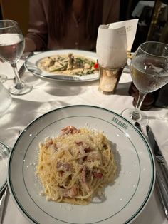 a white plate topped with pasta next to two wine glasses