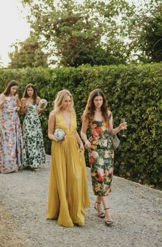 two women in dresses walking down a path with others behind them and one woman wearing a flowered dress