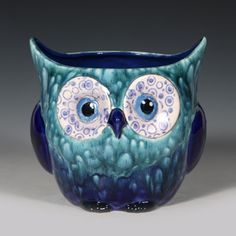 an owl shaped vase with blue and white designs on it's face, sitting in front of a gray background