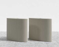 two white vases sitting side by side on a gray tableclothed surface, one with vertical lines in the middle