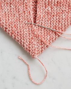 an orange and white knitted piece of cloth next to a pair of knitting needles