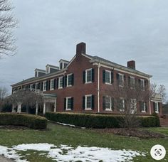 a large red brick house sitting on top of a lush green field covered in snow