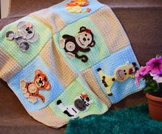 a crocheted blanket with animals on it next to a potted plant and flowers