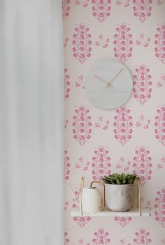 a clock on the wall above a shelf with two cups and a potted plant