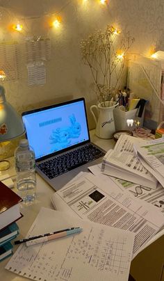 an open laptop computer sitting on top of a desk covered in papers and paperwork next to a bottle of water